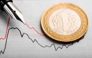 A Turkish lira obscuring an image of a graph showing a downtrend