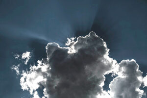 A view of a cloud in the sky with the sun hiding behind it.