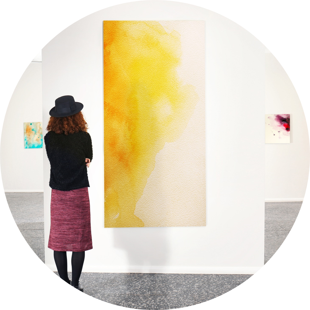 Person looking thoughtfully at a yellow and white painting in an art gallery